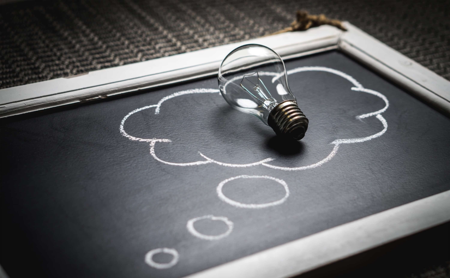 Lightbulb resting on a chalkboard with a drawing of a thought cloud.
