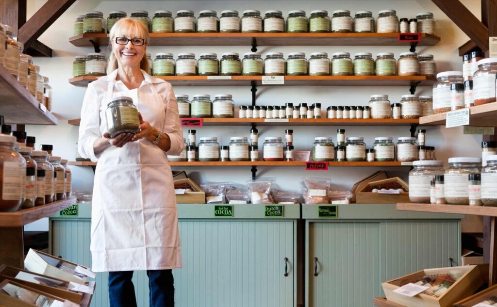 Small business owner smiles in her store while holding a jar of specialty cocoa.