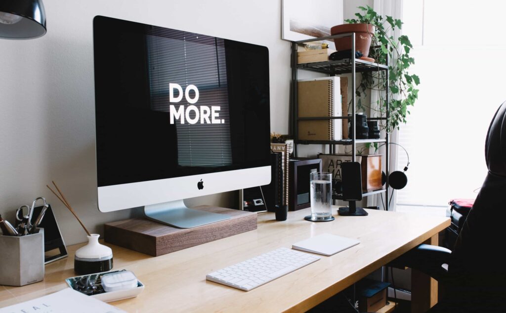 Photo of iMac computer on a desk with a desktop wallpaper that says, "Do More."