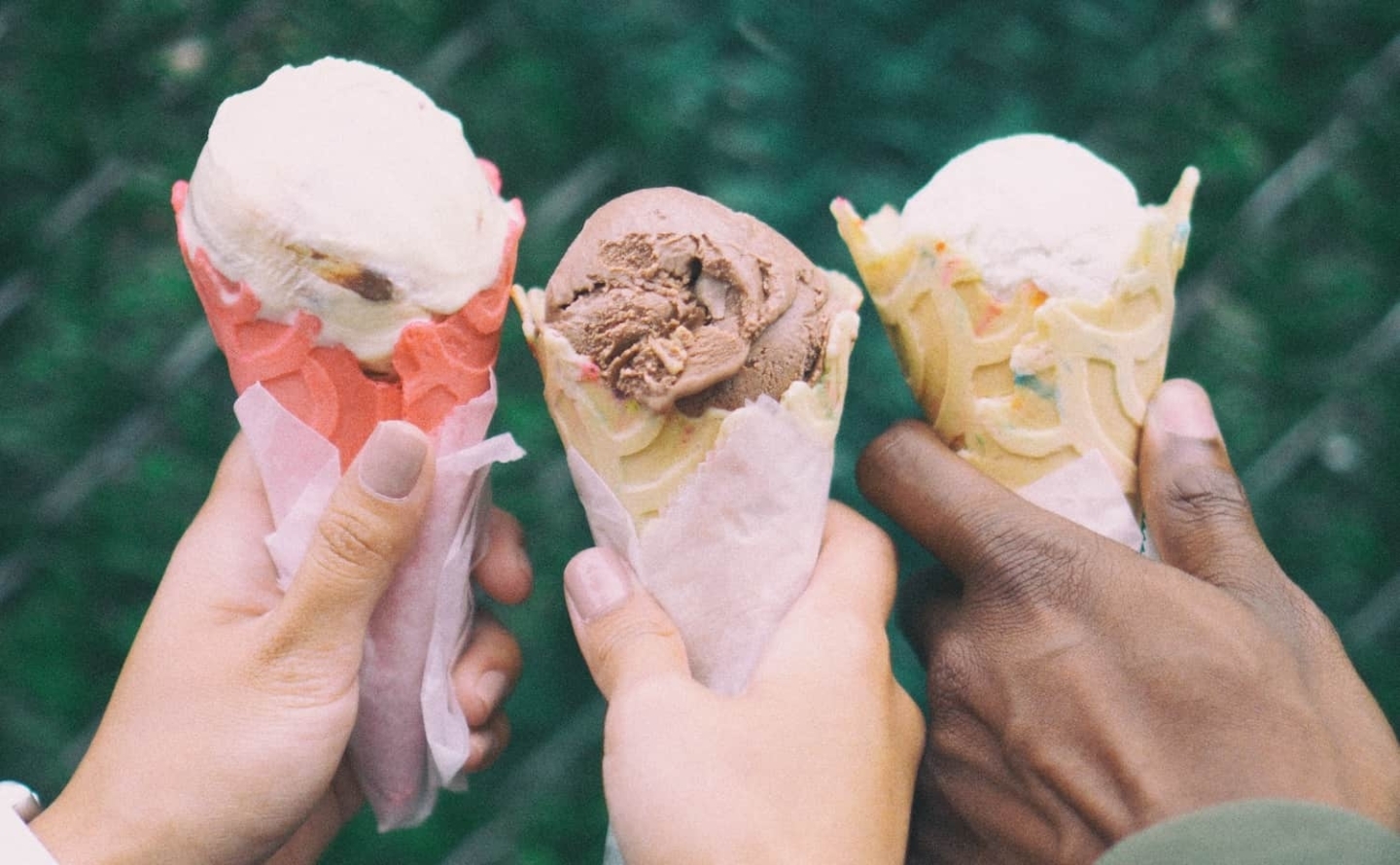 Three hands shown together, each holding a different flavor of ice cream.